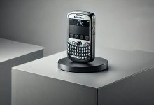 A BlackBerry Pearl 8110 smartphone on a modern desk, showcasing its small size, SureType keyboard, 2MP camera, and trackball navigation system, evoking nostalgia for early smartphone technology.