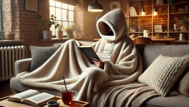 A person lounging on a couch wearing a cozy, oversized wearable blanket with a hood, reading a book and sipping tea. The room has soft lighting and a warm ambiance, highlighting the comfort and practicality of the wearable blanket in a relaxing environment.