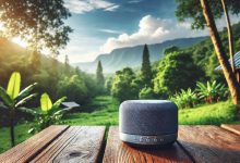 "A modern mini portable speaker on a wooden table outdoors, surrounded by lush greenery and distant mountains under a bright blue sky, creating a peaceful and inviting atmosphere for music enjoyment."