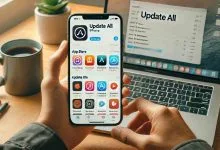 A person holding an iPhone showing the App Store with the "Update All" button visible, displaying various app icons ready to be updated, set against a clean desk setup with a laptop and coffee cup.
